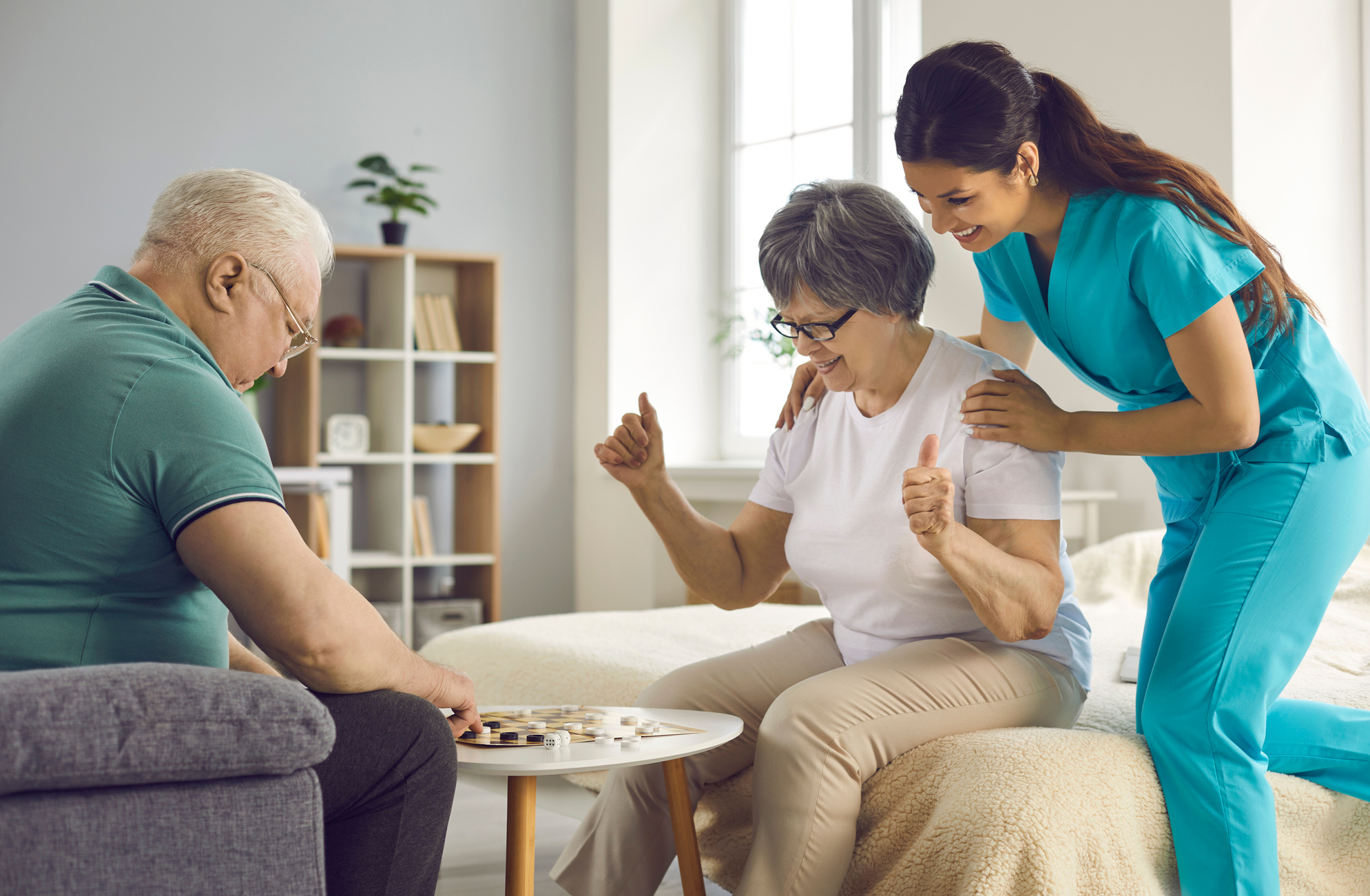 Supportive Care Giver Watching Couple of Her Happy Senior Patients Play Checkers